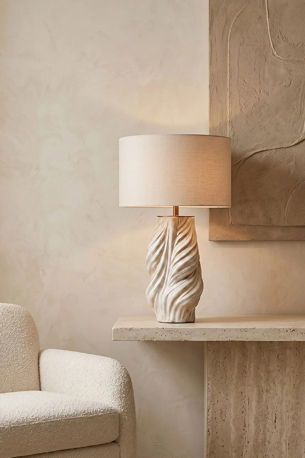 Adara Sculptural Ceramic Table Lamp | Ceramic, Fabric | Displayed on a modern floating travertine ledge next to a cream armchair against a minimalist textured plaster wall nook | Samu Lamp
