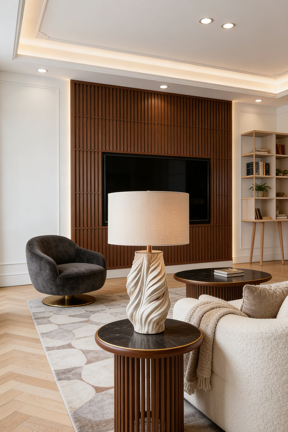 Adara Sculptural Ceramic Table Lamp | Ceramic, Fabric | Positioned on a round wooden end table next to a cream sofa in a contemporary living room with a dark wood media wall | Samu Lamp