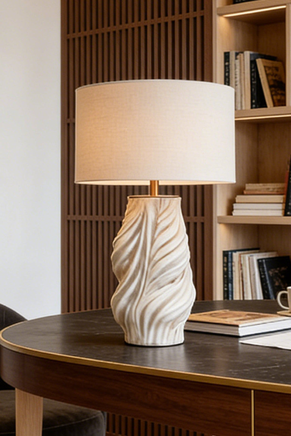 Adara Sculptural Ceramic Table Lamp | Ceramic, Fabric | Staged nicely on a dark polished oval wood desk or boardroom table near a vertical wood slat wall divider | Samu Lamp