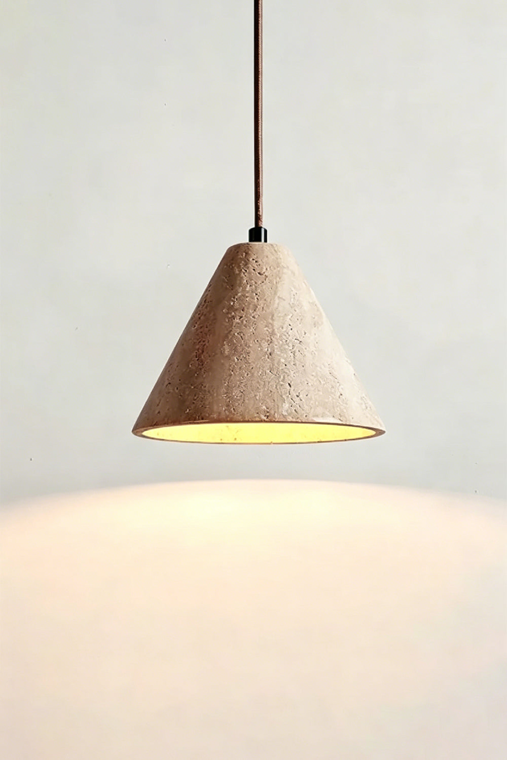 Lit Aethel Core Pendant Light | Beige Travertine, Metal | Wall view showing warm downward glow | Samu Lamp
