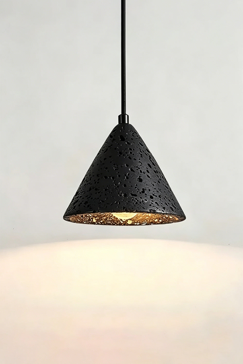 Lit Aethel Core Pendant Light | Black Travertine, Metal | Wall view showing textured stone and illumination | Samu Lamp