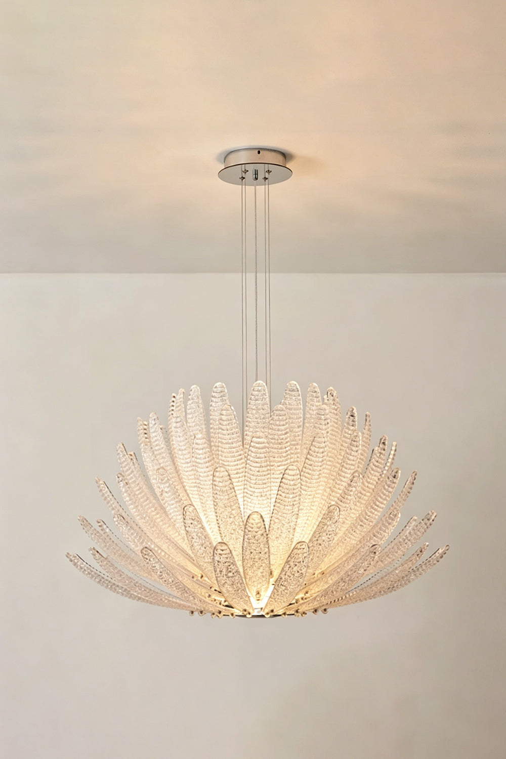 Helios Agave Glass Starburst Chandelier | Glass, Metal | Clear glass variant lit against a light neutral wall, creating a soft white ambiance | Isolated shot | Samu Lamp