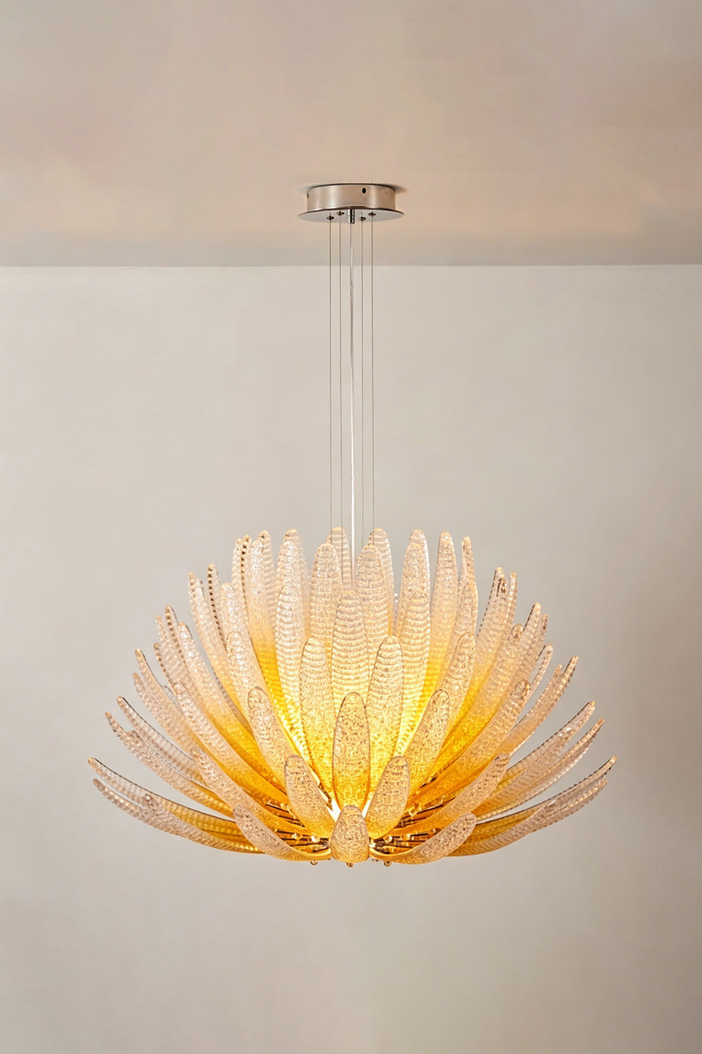 Helios Agave Glass Starburst Chandelier | Glass, Metal | Amber glass variant lit against a light neutral wall, showing its warm golden tones | Isolated shot | Samu Lamp