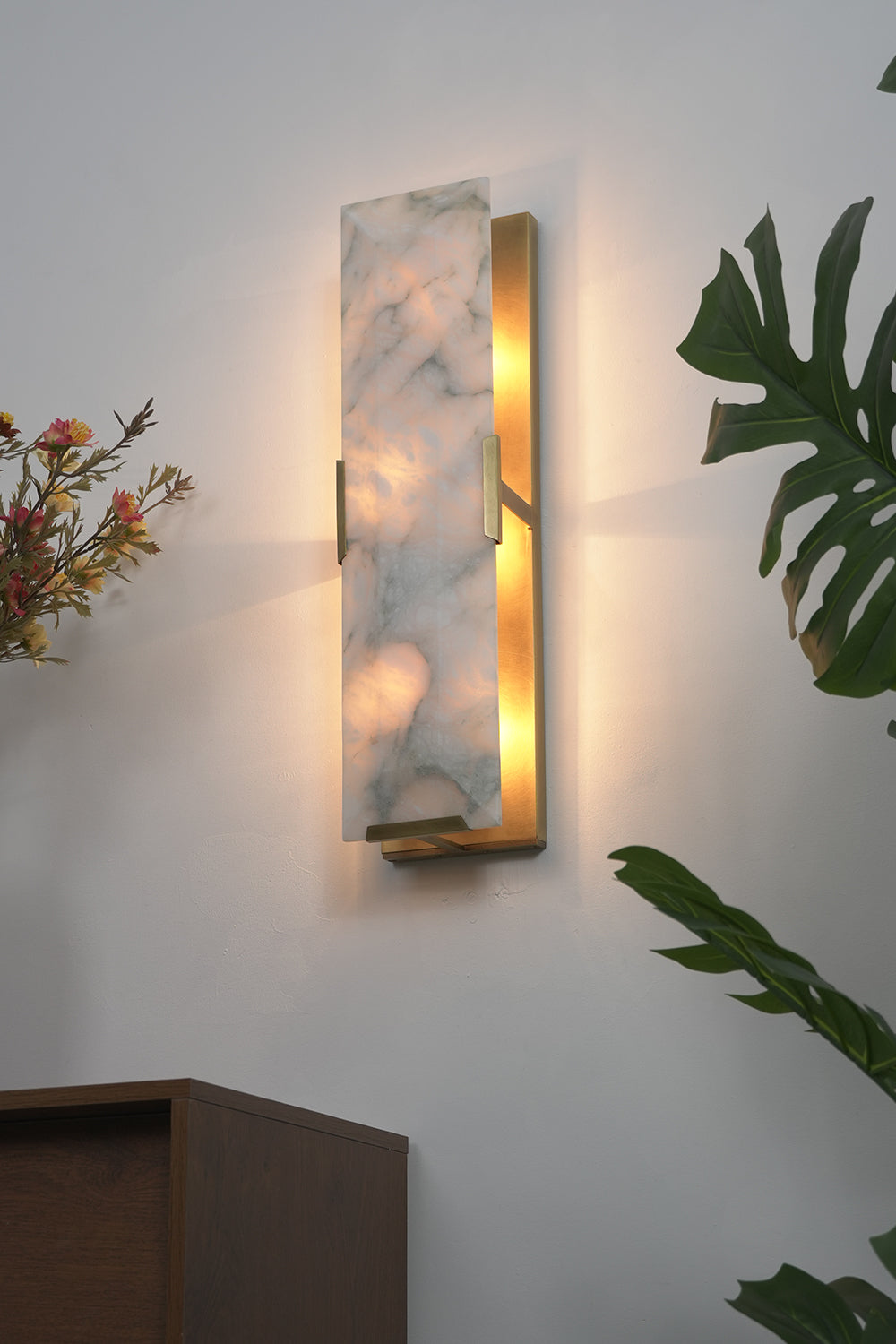 Lit alabaster wall lamp with 3-tier design | Brass, Alabaster | Side perspective view in a living room near plants | Samu Lamp