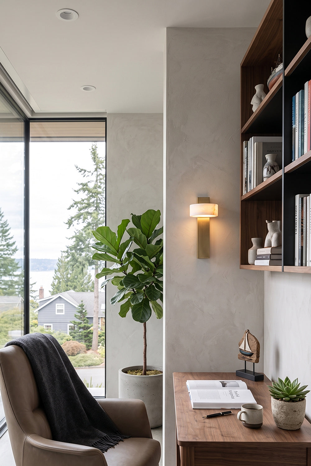 Alaric Alabaster Bar Wall Sconce | Natural Alabaster and Brass | Fixed on a home office wall next to a large dark wood bookshelf and a cozy leather armchair | Samu Lamp