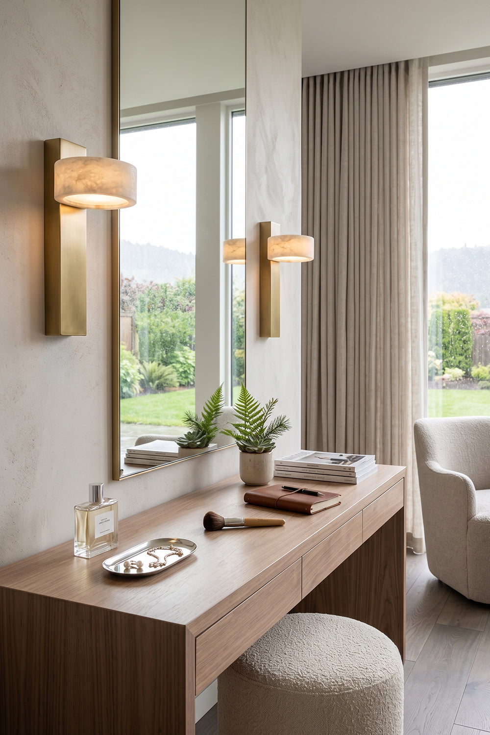 Alaric Alabaster Bar Wall Sconce | Natural Alabaster and Brass | Installed on a wall panel next to a large mirror in an elegant vanity makeup area with a stool | Samu Lamp