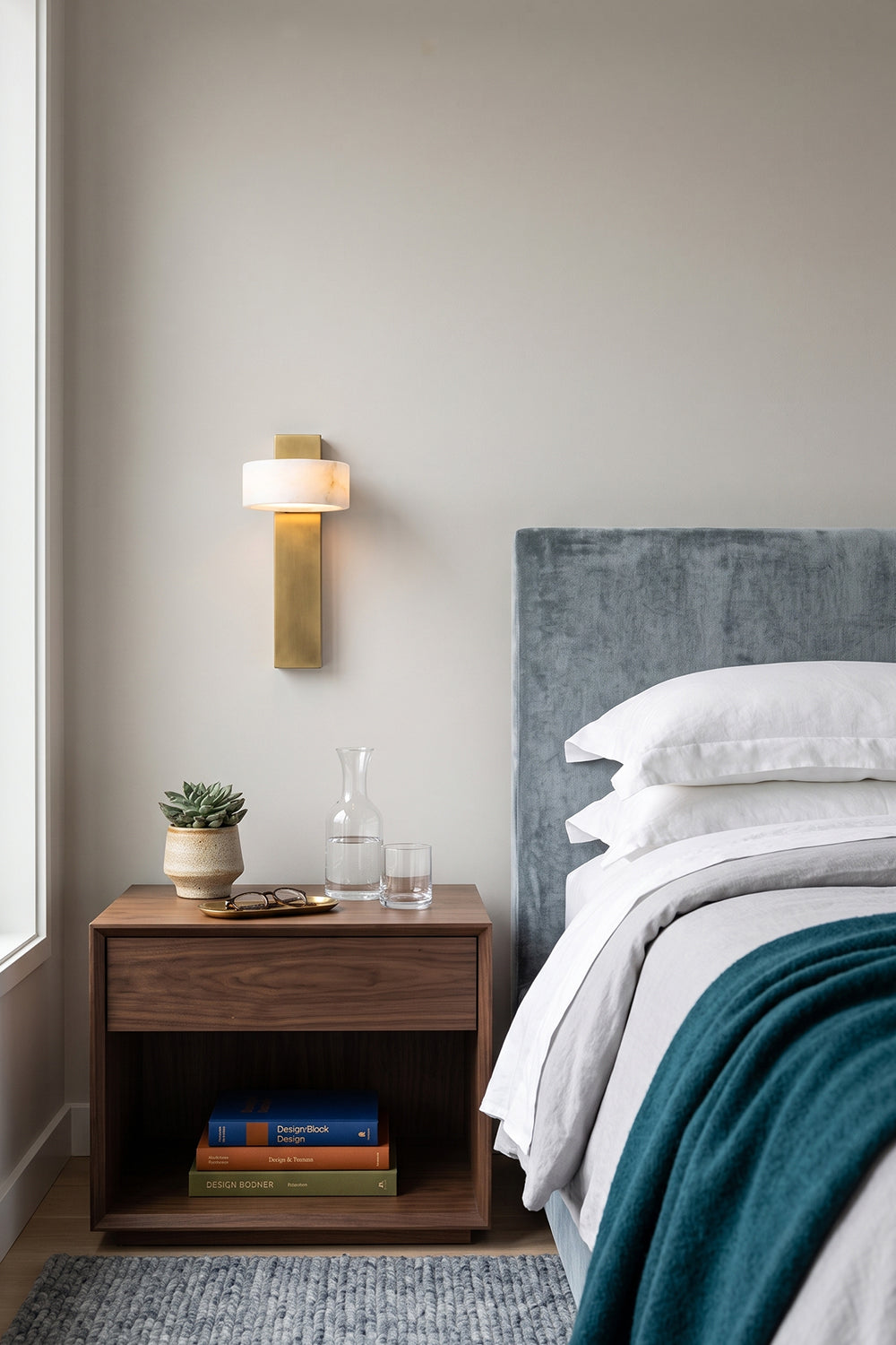 Alaric Alabaster Bar Wall Sconce | Natural Alabaster and Brass | Mounted on a bedroom wall next to a cozy bed with a teal blanket above a dark wooden nightstand | Samu Lamp