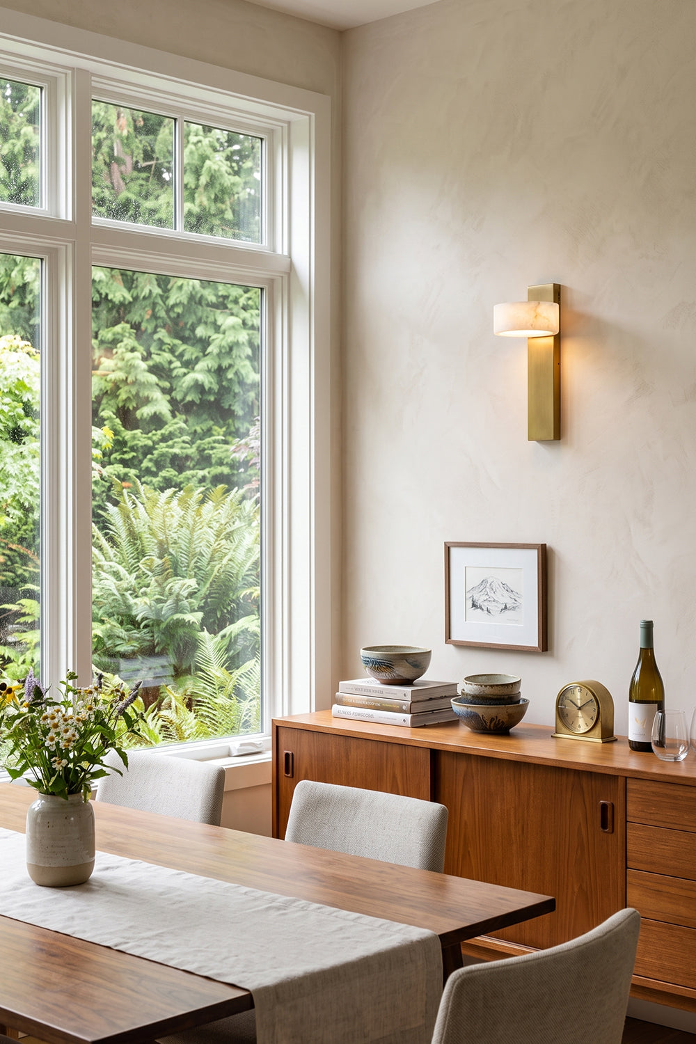 Alaric Alabaster Bar Wall Sconce | Natural Alabaster and Brass | Positioned on a dining room wall near large windows showcasing a modern wooden table and chairs setup | Samu Lamp