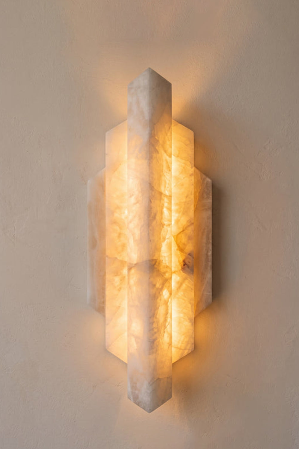 Alaric Tiered Alabaster Wall Sconce | Natural Alabaster and Metal | Front view of the glowing art deco stone sconce casting a soft light on a light neutral wall | Samu Lamp