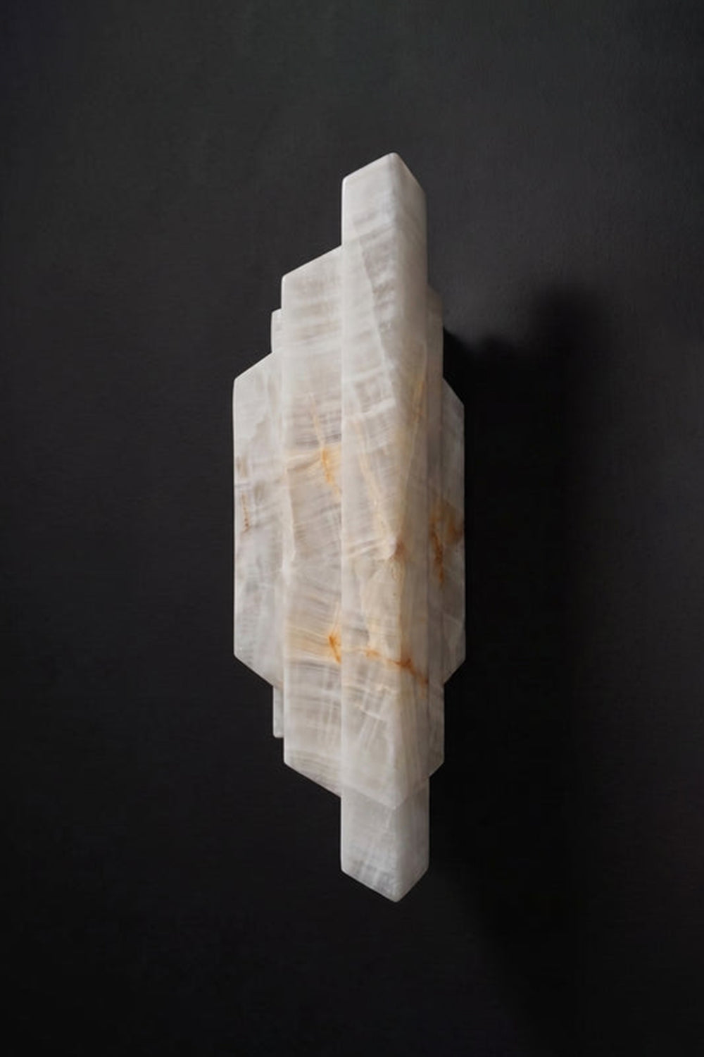 Alaric Tiered Alabaster Wall Sconce | Natural Alabaster and Metal | Side profile shot of the unlit tiered white stone block lamp against a solid matte black background | Samu Lamp