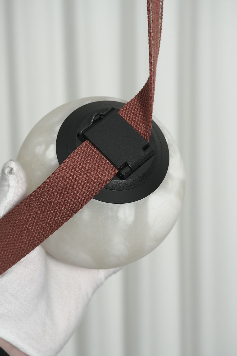 Albiane Draped Chandelier | Alabaster and Woven Strap | Gloved hand holding unlit alabaster globe and strap | Samu Lamp