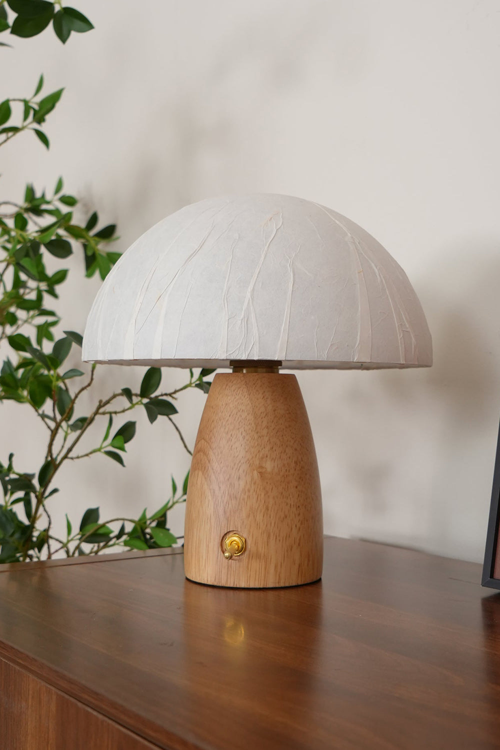 Alice Mushroom Table Lamp | Wood, Glass | Close-up shot of the lit mushroom lamp on a rich dark wood desk next to climbing green plant vines | Samu Lamp