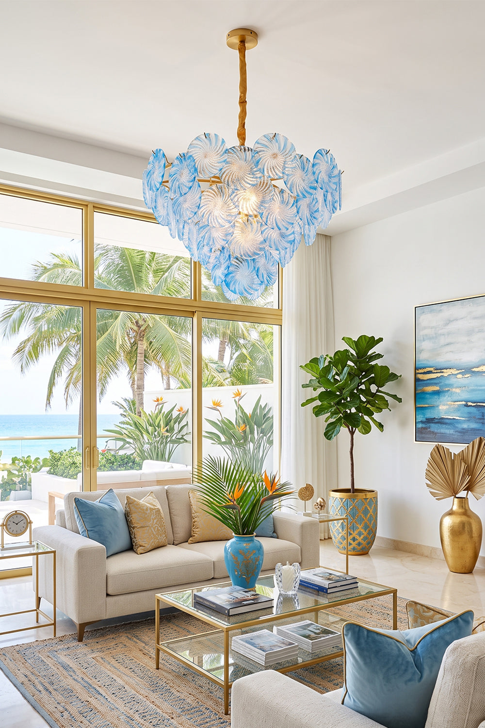 Amara Pink Glass Petal Chandelier | Coastal Living Room | The light blue petal chandelier casting a soft glow in a spacious tropical lounge area with palm tree window views | Samu Lamp