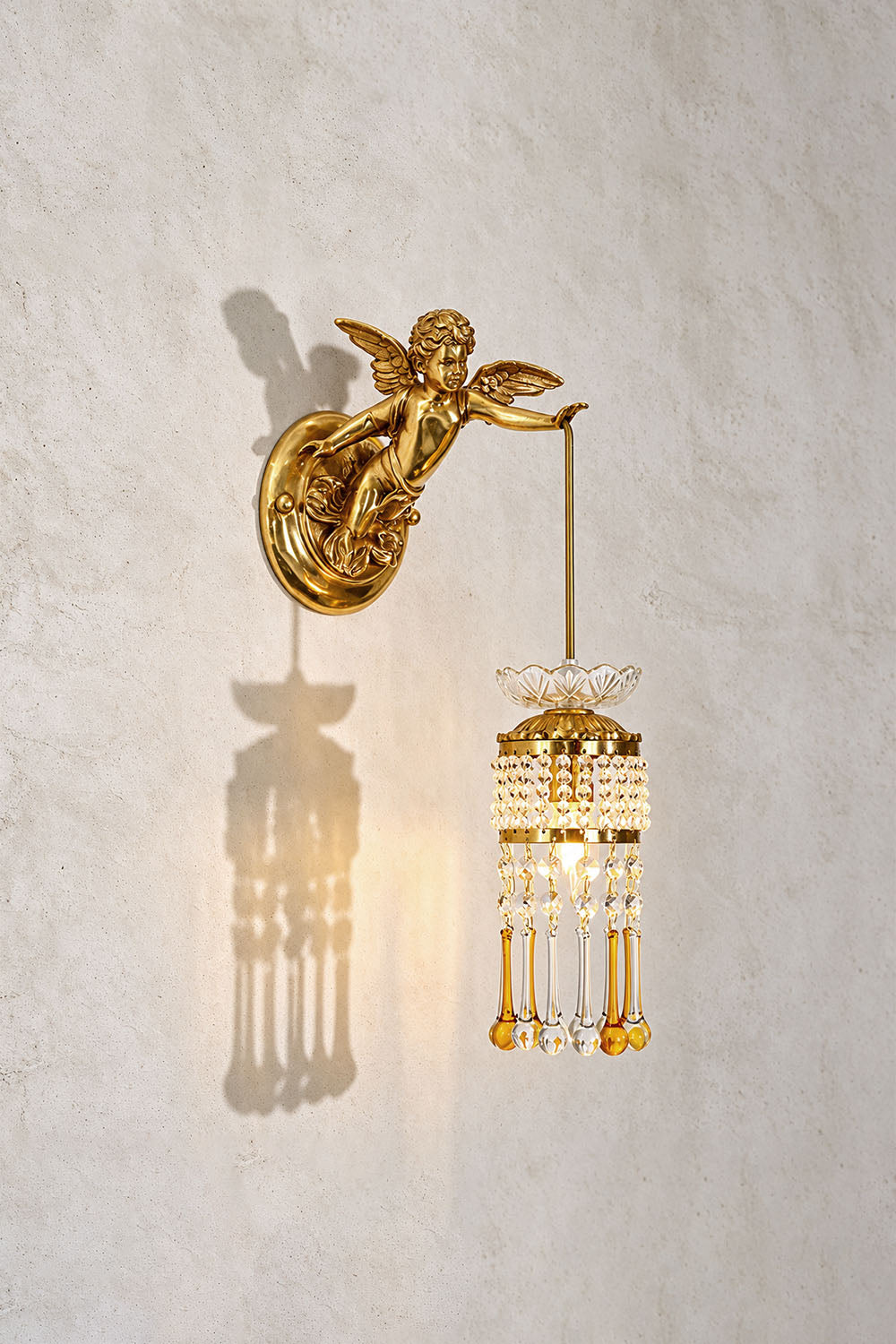 Ambrelise Cherub Wall Sconce | Cast Brass and K9 Crystal | Angled view on plaster wall casting warm radiant glow | Samu Lamp