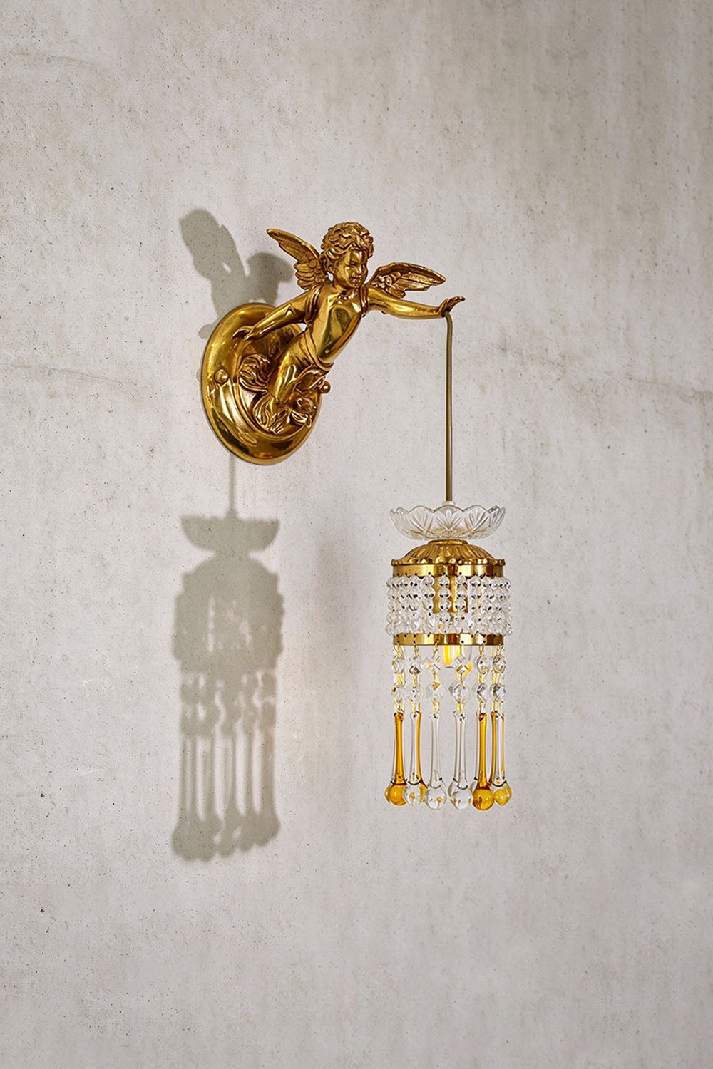Ambrelise Cherub Wall Sconce | Brass and Faceted Crystal | Angled perspective on grey textured wall, unlit state | Samu Lamp