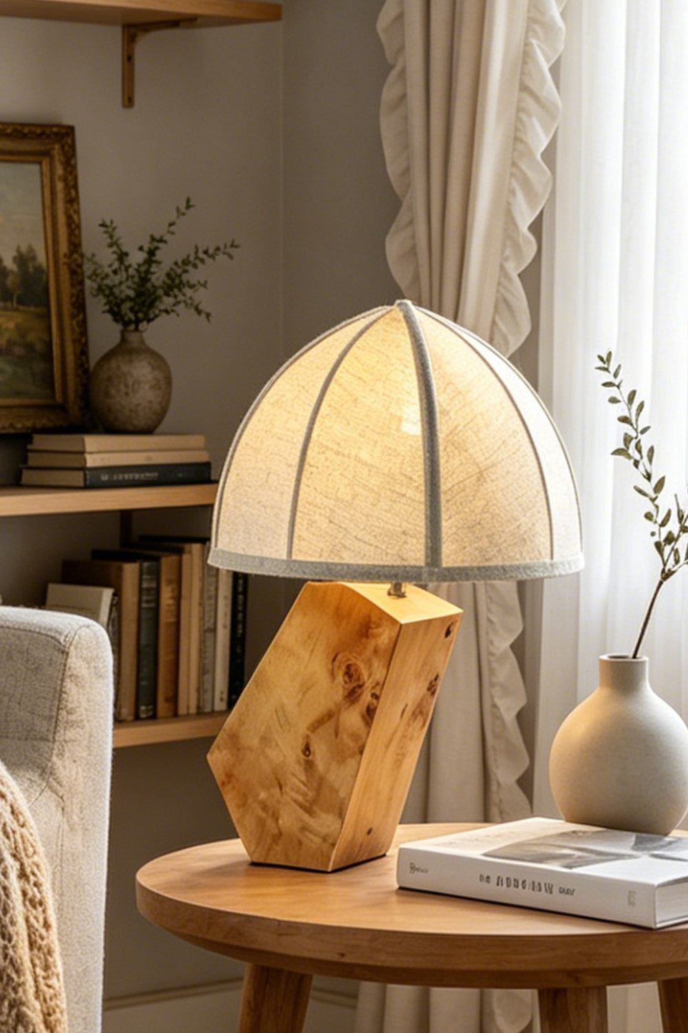 Angolo Canted Faceted Wood Table Lamp | Wood, Fabric, Metal | Sitting on a round wooden end table next to a sofa and airy curtains, casting soft ambient light | Samu Lamp