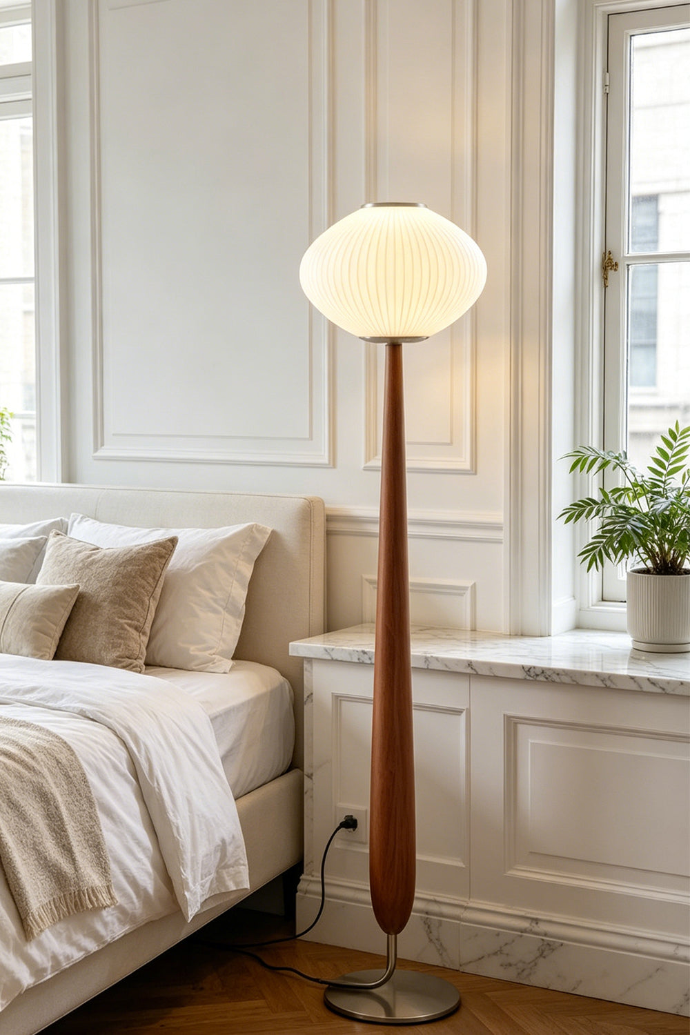 Arden Walnut Floor Lamp | Wood, Metal, Fabric | Providing soft bedtime ambient illumination in a cozy bedroom corner next to a cream platform bed and white paneled walls | Samu Lamp