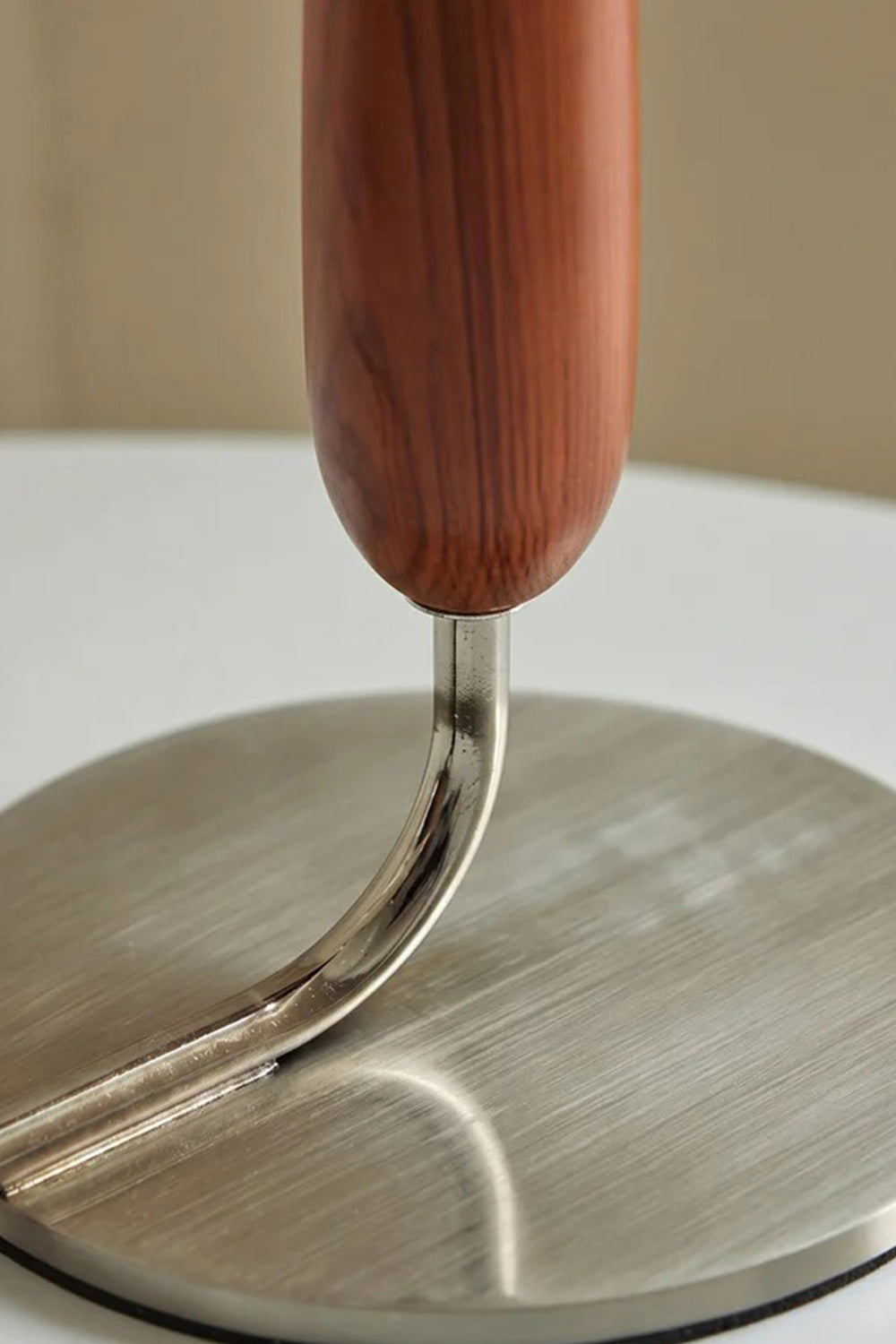 Arden Walnut Floor Lamp | Wood, Metal, Fabric | Macro structural view showing the curved metallic neck pipe connecting the walnut wood stem to the circular brushed metal base plate | Detail shot | Samu Lamp