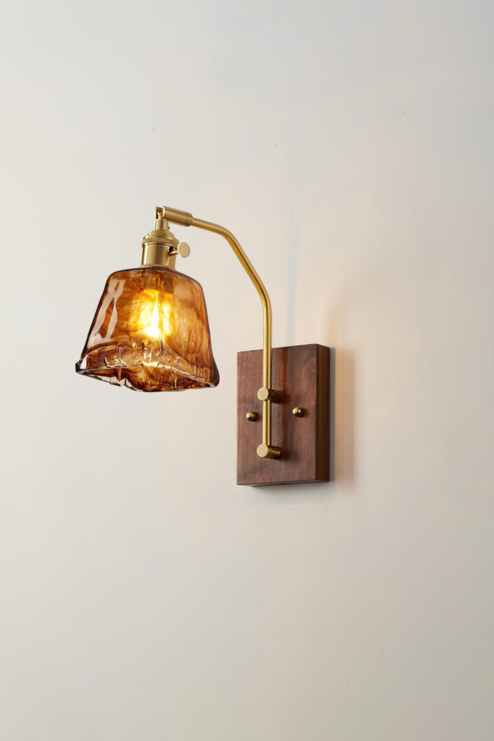 Arlo Amber Ripple Wall Lamp | Glass, Metal, Wood | Side angled perspective of the glowing glass wall lamp projecting a comforting light halo on a white wall | Samu Lamp