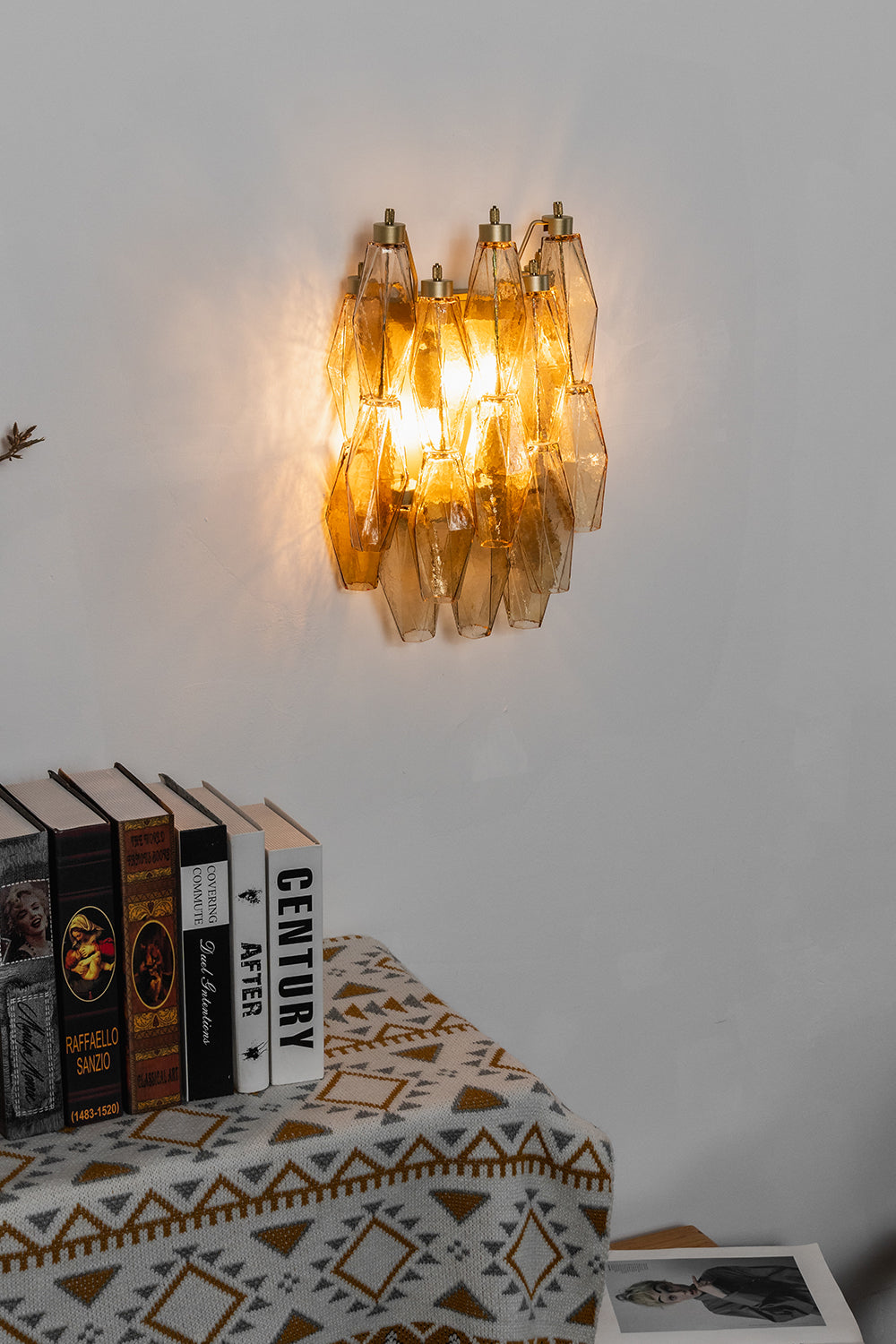 Lit amber Art Poliedri wall sconce | Metal, Glass | Centered on a white wall above a wooden cabinet | Samu Lamp