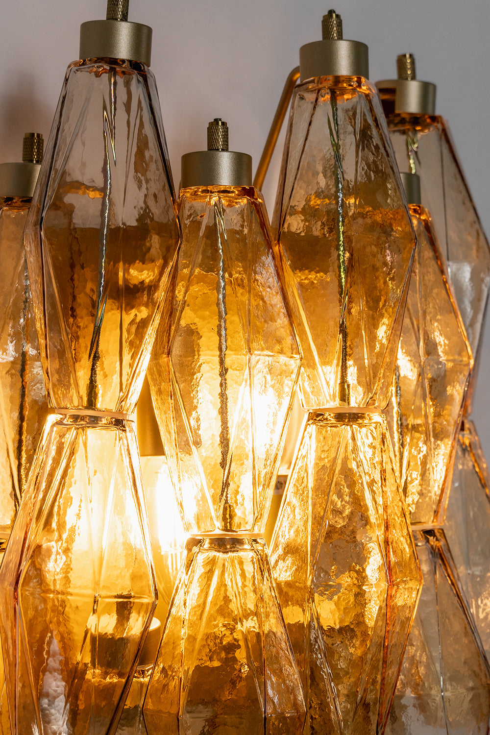 Close-up of lit amber polyhedral glass | Metal, Glass | Detail view of the warm glow and multifaceted glass prisms | Samu Lamp