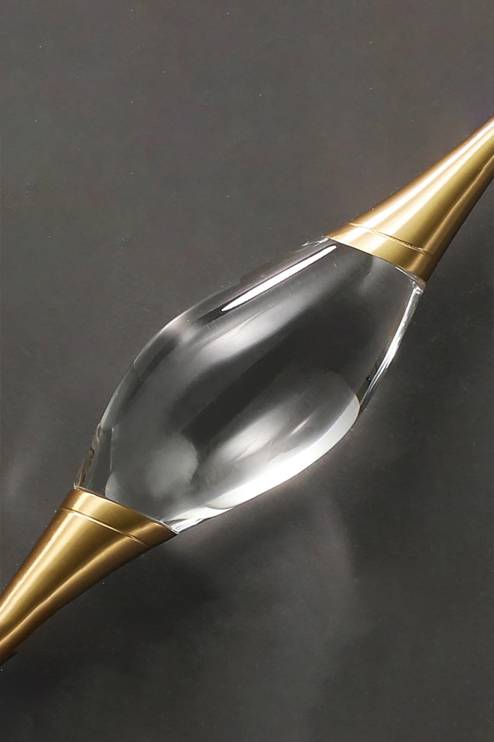 Astraea Crystal Linear Wall Sconce | Crystal, Brass | Macro close-up detail of the clear sculpted crystal core and the sleek gold brass conical holder on a dark background | Detail shot | Samu Lamp