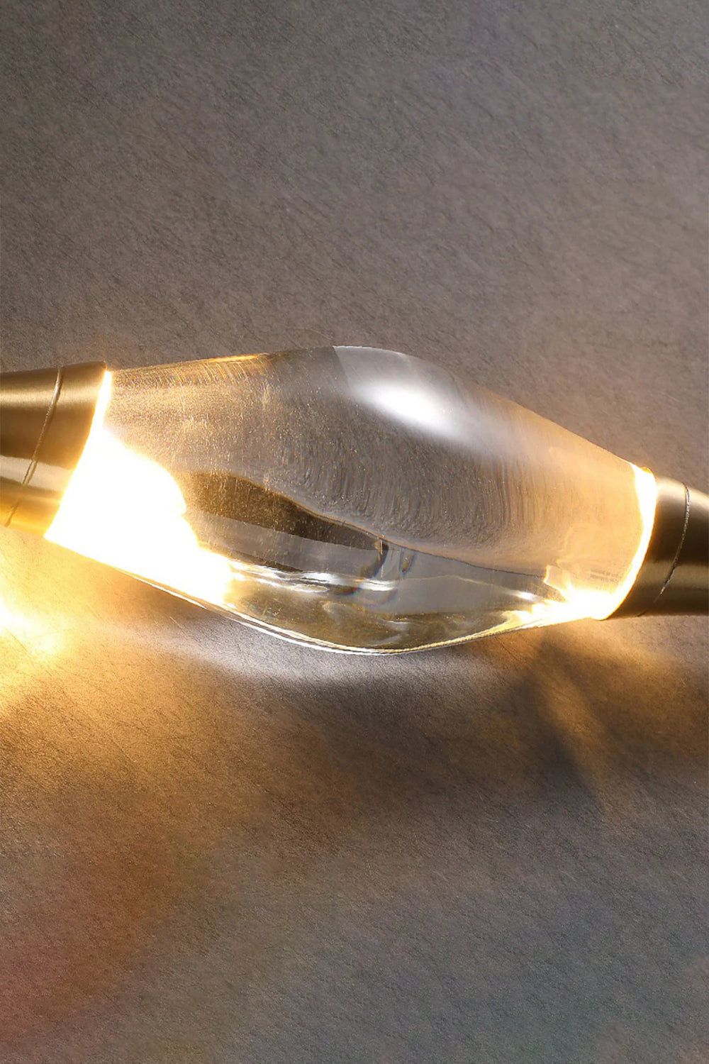 Astraea Crystal Linear Wall Sconce | Crystal, Brass | Close-up illuminated view focusing on the warm light refracting and reflecting through the thick faceted clear crystal center | Detail shot | Samu Lamp
