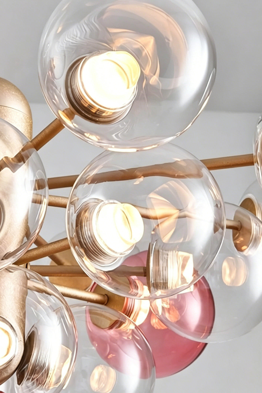 Astraea Prismatic Globe Chandelier | Glass, Metal | Close-up focus on the illuminated clear and pink glass sphere globes showcasing the light transmission and bubble cluster effect | Detail shot | Samu Lamp