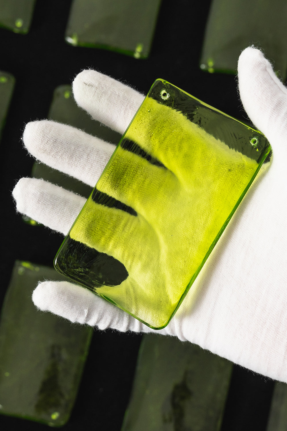 Aura Verdant Tiered Green Glass Ceiling Light | Metal, Glass | A white-gloved hand holding a single translucent textured green glass plate to show its color and transparency | Detail shot | Samu Lamp