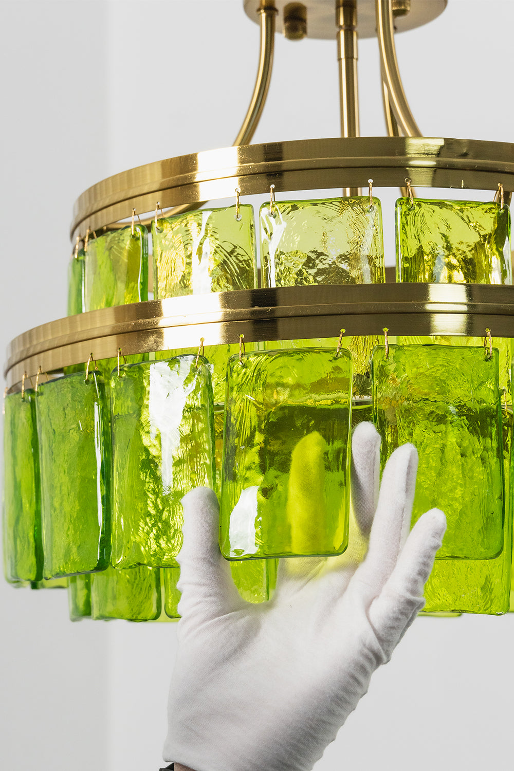 Aura Verdant Tiered Green Glass Ceiling Light | Metal, Glass | A white-gloved hand adjusting the bottom section of the two-tier green glass fixture | Detail shot | Samu Lamp