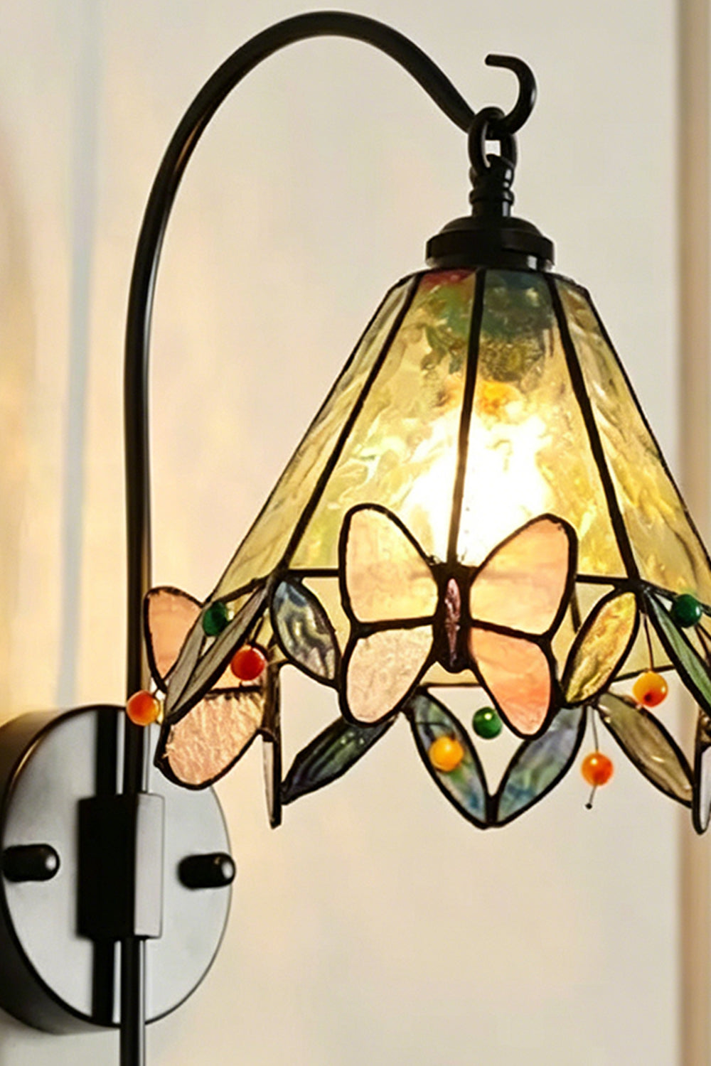 Aura Vine Stained Glass Wall Sconce | Glass, Metal | Close-up side profile of the illuminated wall lamp showing the curved black arm, mount base, and glowing glass panels | Detail shot | Samu Lamp
