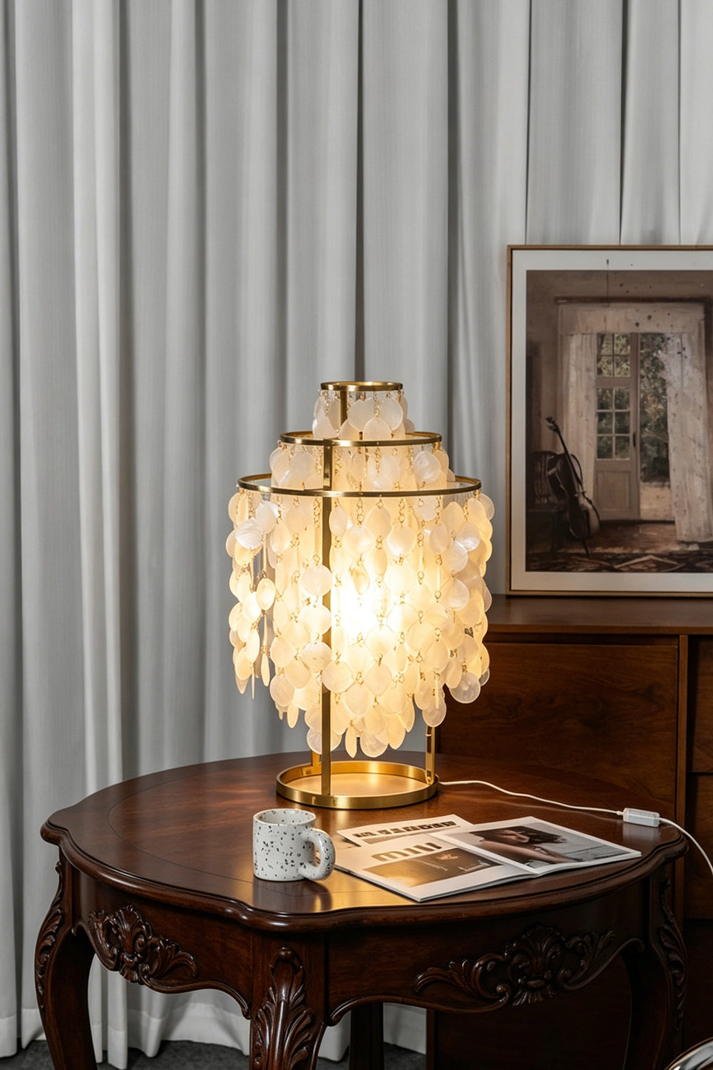 Aurelia Tiered Capiz Table Lamp | Capiz Shell, Metal | Placed on a round antique wooden table, casting a warm ambient light in a cozy dining space | Samu Lamp