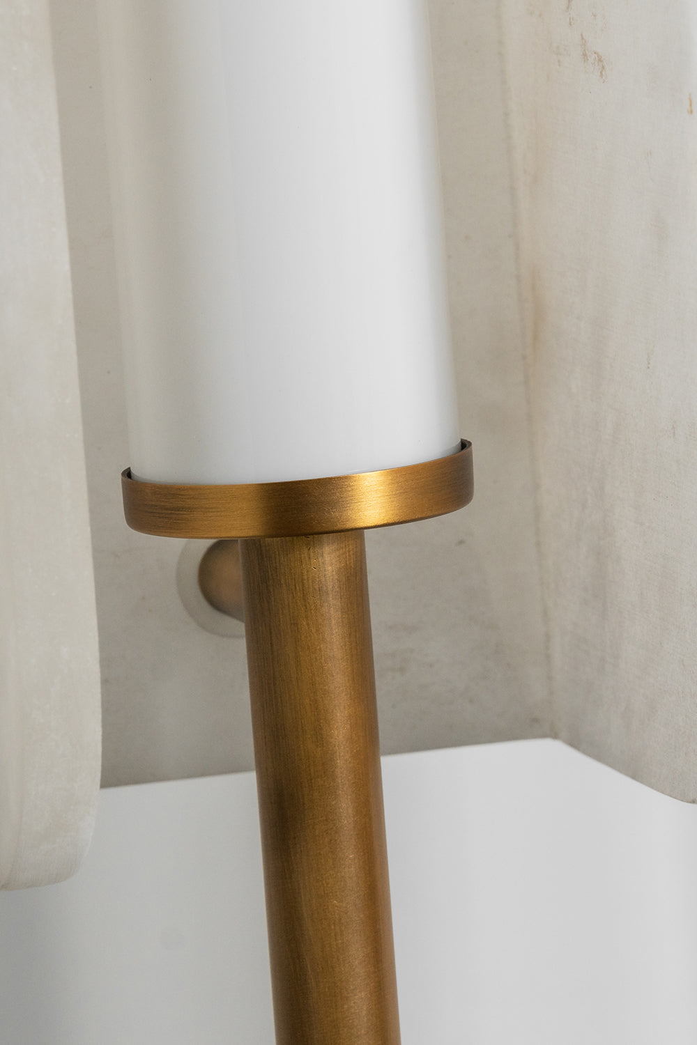 Aurelius Alabaster Brass Floor Lamp | Alabaster, Brass | Detailed shot showing the connection point where the slim vertical gold brass rod meets the base of the cylindrical white light diffuser | Detail shot | Samu Lamp