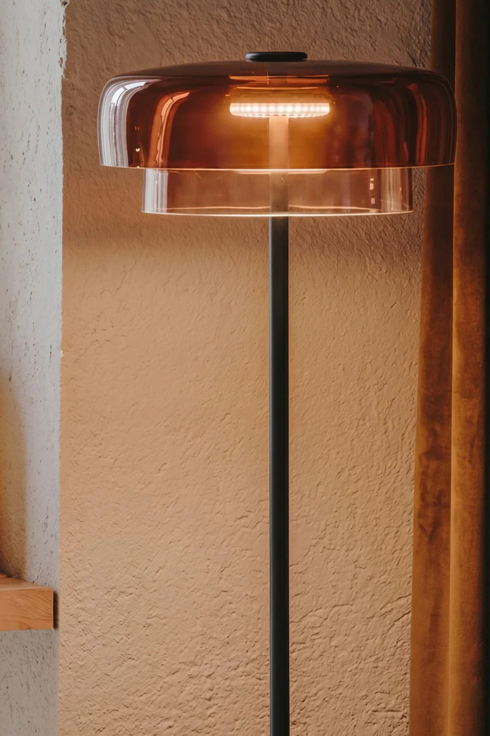 Aven Minimalist Architectural Floor Lamp | Glass, Metal | Close-up shot of the amber glass shade variant casting a warm golden glow against a textured neutral wall | Detail shot | Samu Lamp