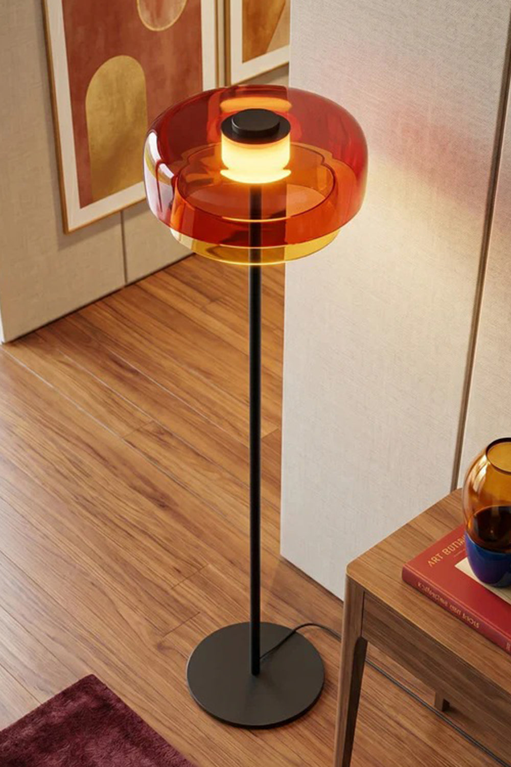 Aven Minimalist Architectural Floor Lamp | Glass, Metal | Elevated angled close-up view of the glowing orange glass variant standing elegantly on a dark wood parquet floor | Detail shot | Samu Lamp