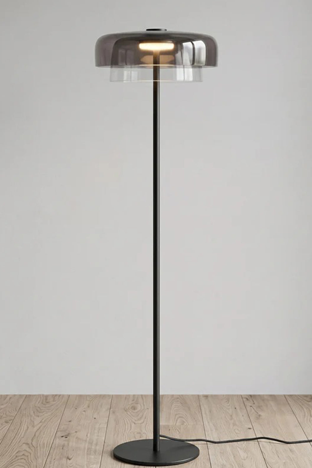Aven Minimalist Architectural Floor Lamp | Glass, Metal | Studio front view of the fully illuminated smoky grey glass floor lamp variant displayed on a clean wooden floor | Samu Lamp