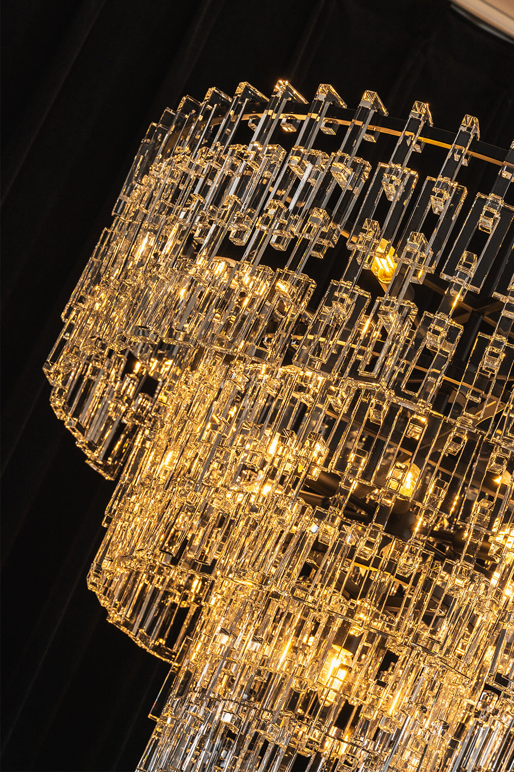 Aven Tiered Glass Prism Chandelier | Glass, Metal | Dramatic close-up under low lighting showing the crystal tiers radiating an intense, warm golden light halo | Detail shot | Samu Lamp