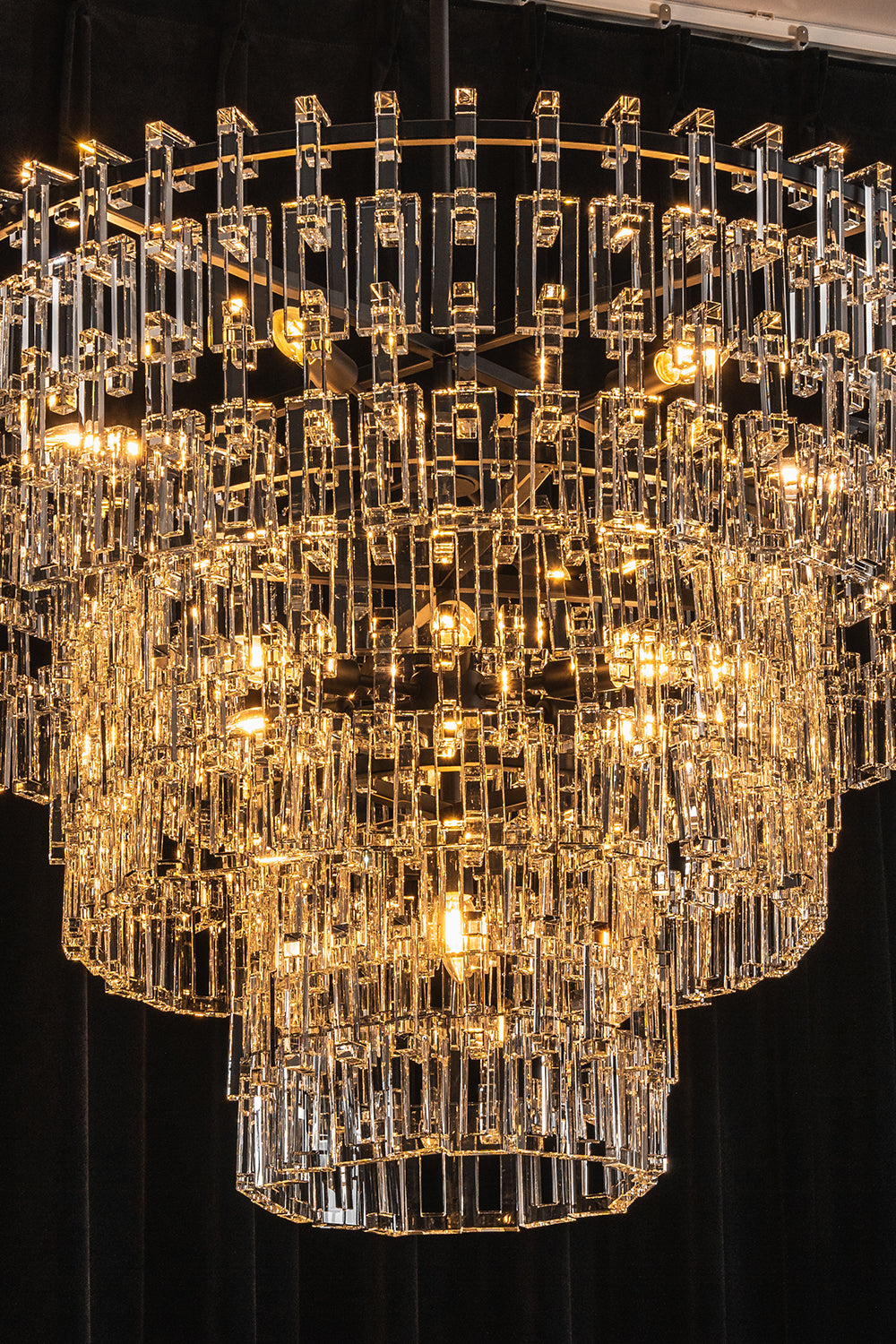 Aven Tiered Glass Prism Chandelier | Glass, Metal | Close-up studio shot of the illuminated chandelier tiers filled with sparkling warm yellow ambient light | Samu Lamp