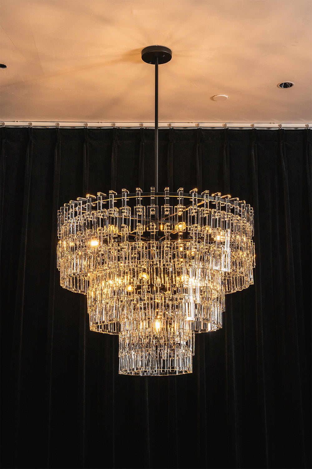 Aven Tiered Glass Prism Chandelier | Glass, Metal | Centered view of the fully illuminated black tier variant casting warm ambient light against a solid dark backdrop | Samu Lamp