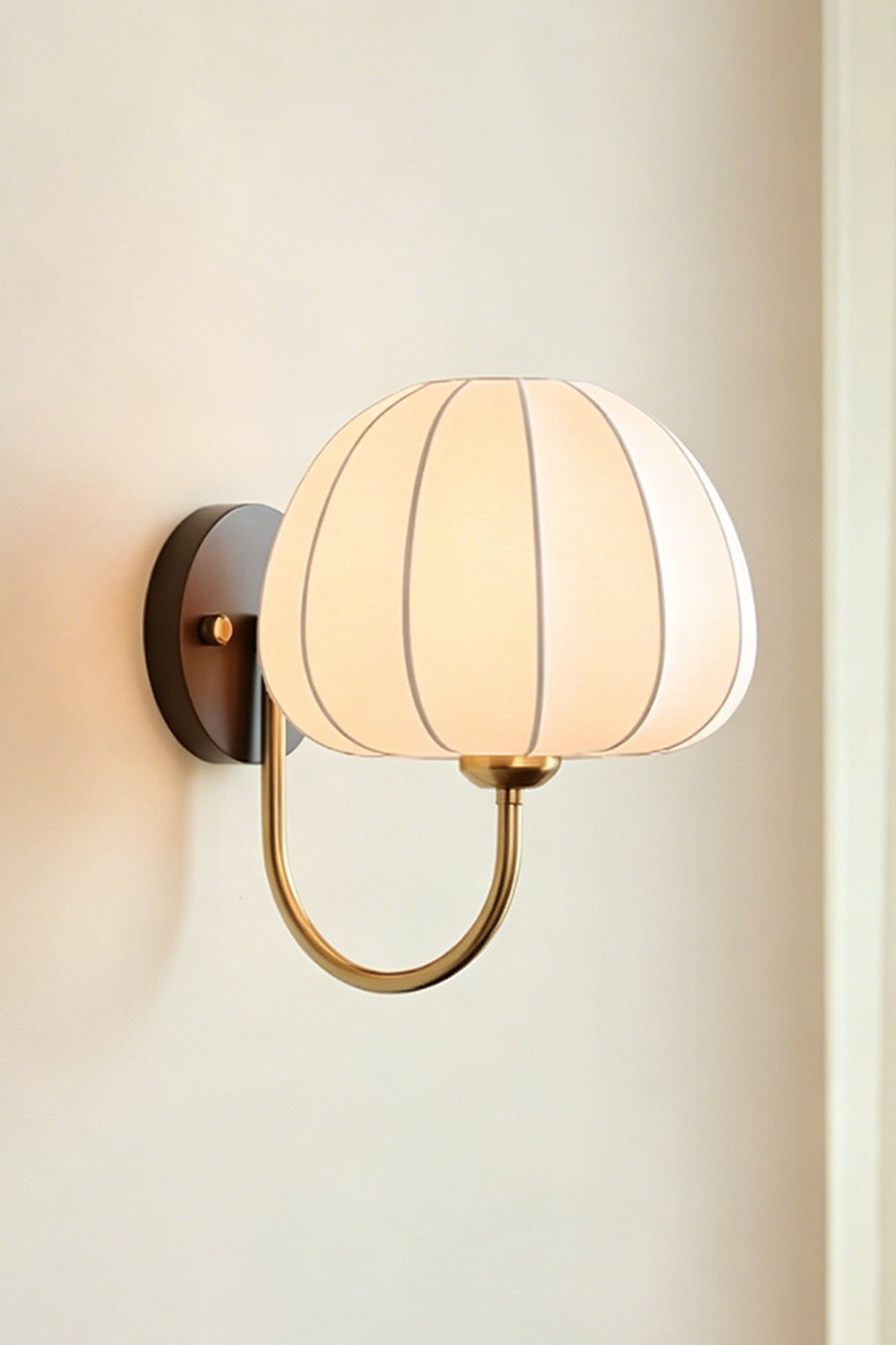 Baird Mid Century Pumpkin Wall Lamp | Metal, Fabric, Wood | Frontal angled view of the fully lit lamp radiating soft light against a neutral plain wall | Isolated shot | Samu Lamp