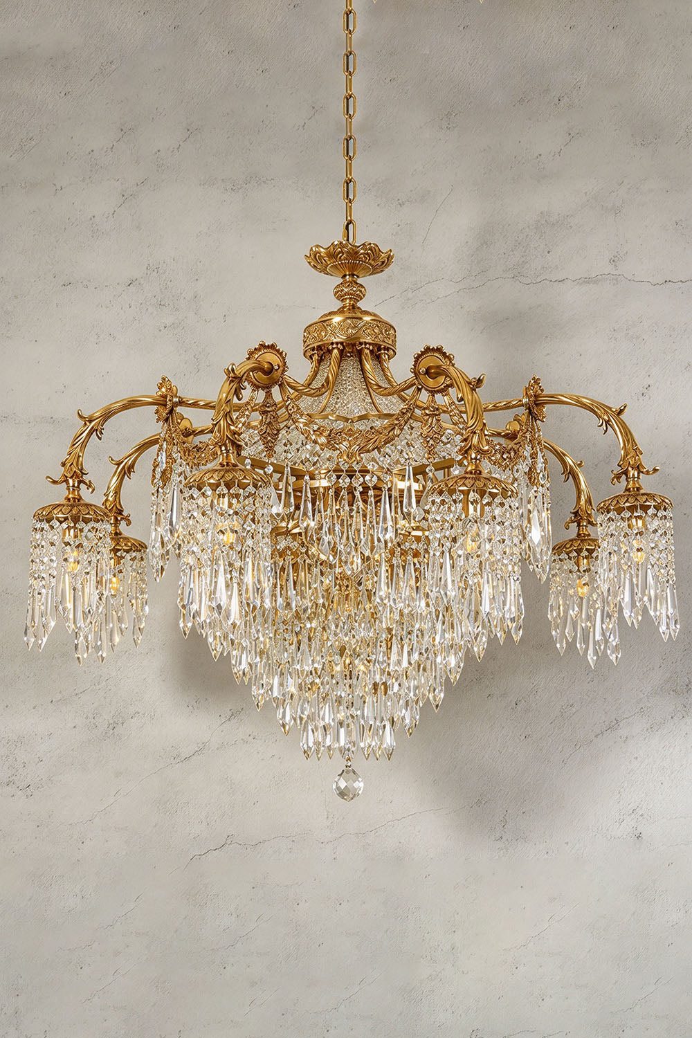 Belcastre Brass Crowned Crystal Cascade Chandelier | Cut Crystal and Brass | Illuminated product view glowing brightly against a textured wall | Samu Lamp