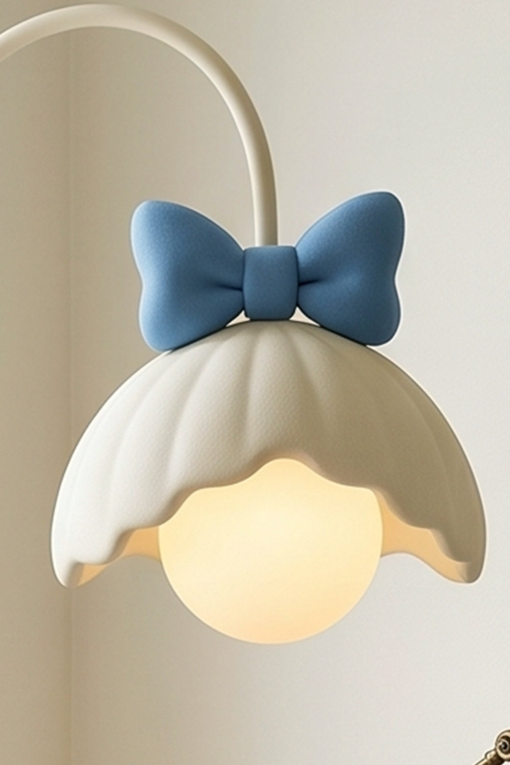 Bella Bow Arched Floor Lamp | Metal, Resin | Close-up view of the lit blue bow variant radiating a soft warm light from beneath its white flower-shaped shade | Detail shot | Samu Lamp