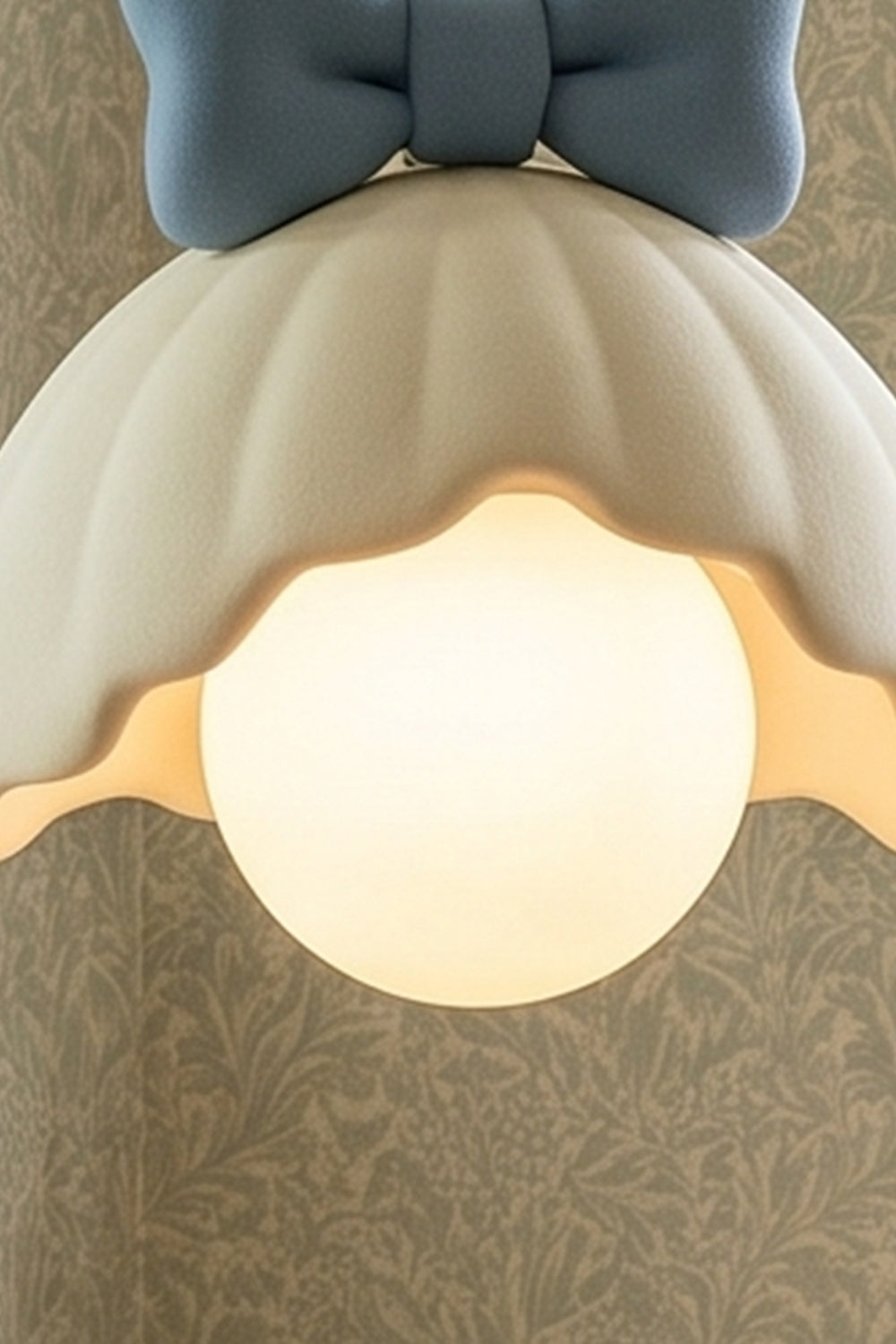 Bella Bow Arched Floor Lamp | Metal, Resin | Upward angled close-up view showing the warm spherical bulb illuminated under the blue bow scalloped shade structure | Detail shot | Samu Lamp