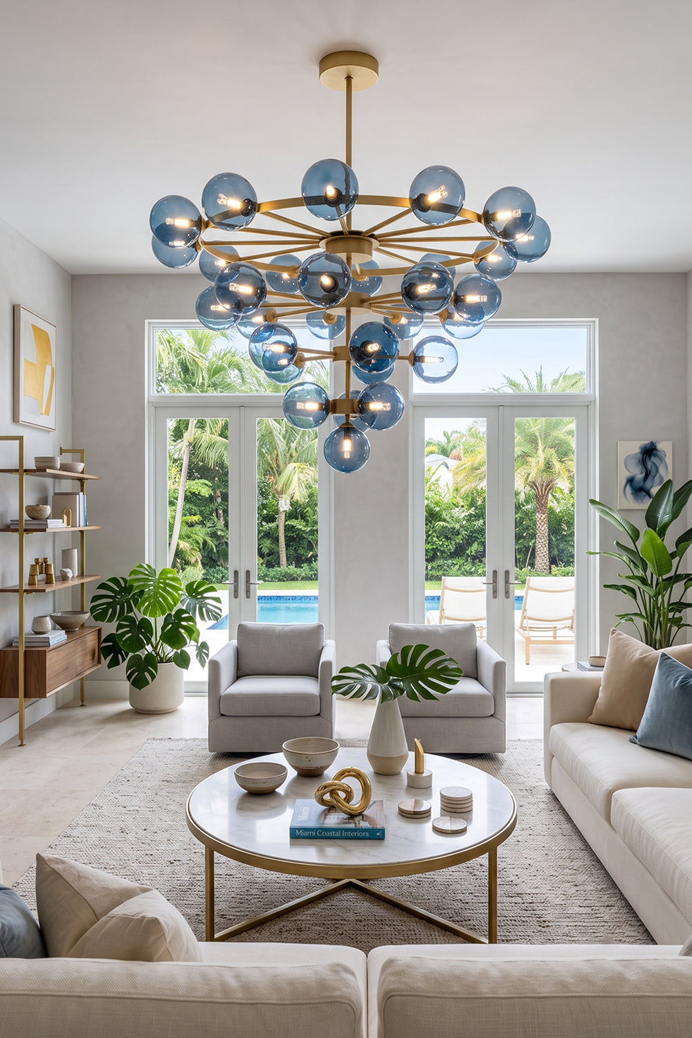 Blue Glass Bubble Globe Tiered Chandelier | Blue Glass and Brass Metal | Illuminating a bright coastal living room with a cream sofa and gold coffee table | Samu Lamp