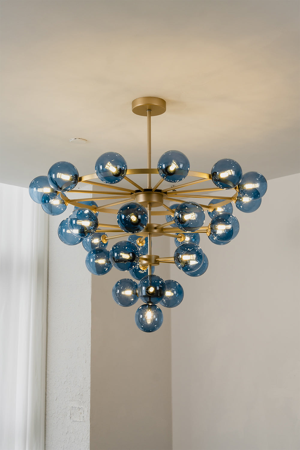 Blue Glass Bubble Globe Tiered Chandelier | Blue Glass and Brass Metal | Full view of the fixture hanging from the ceiling in a modern home interior setting | Samu Lamp