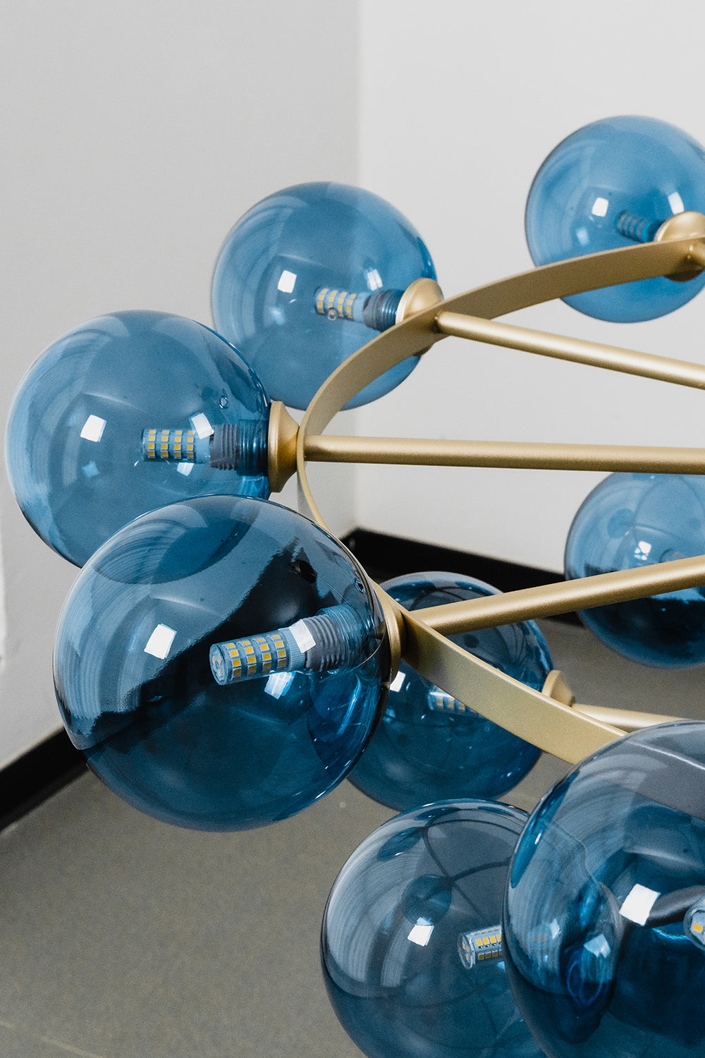 Blue Glass Bubble Globe Tiered Chandelier | Blue Glass and Brass Metal | Close-up side perspective focusing on a cluster of blue bubble globes and brass rods | Samu Lamp