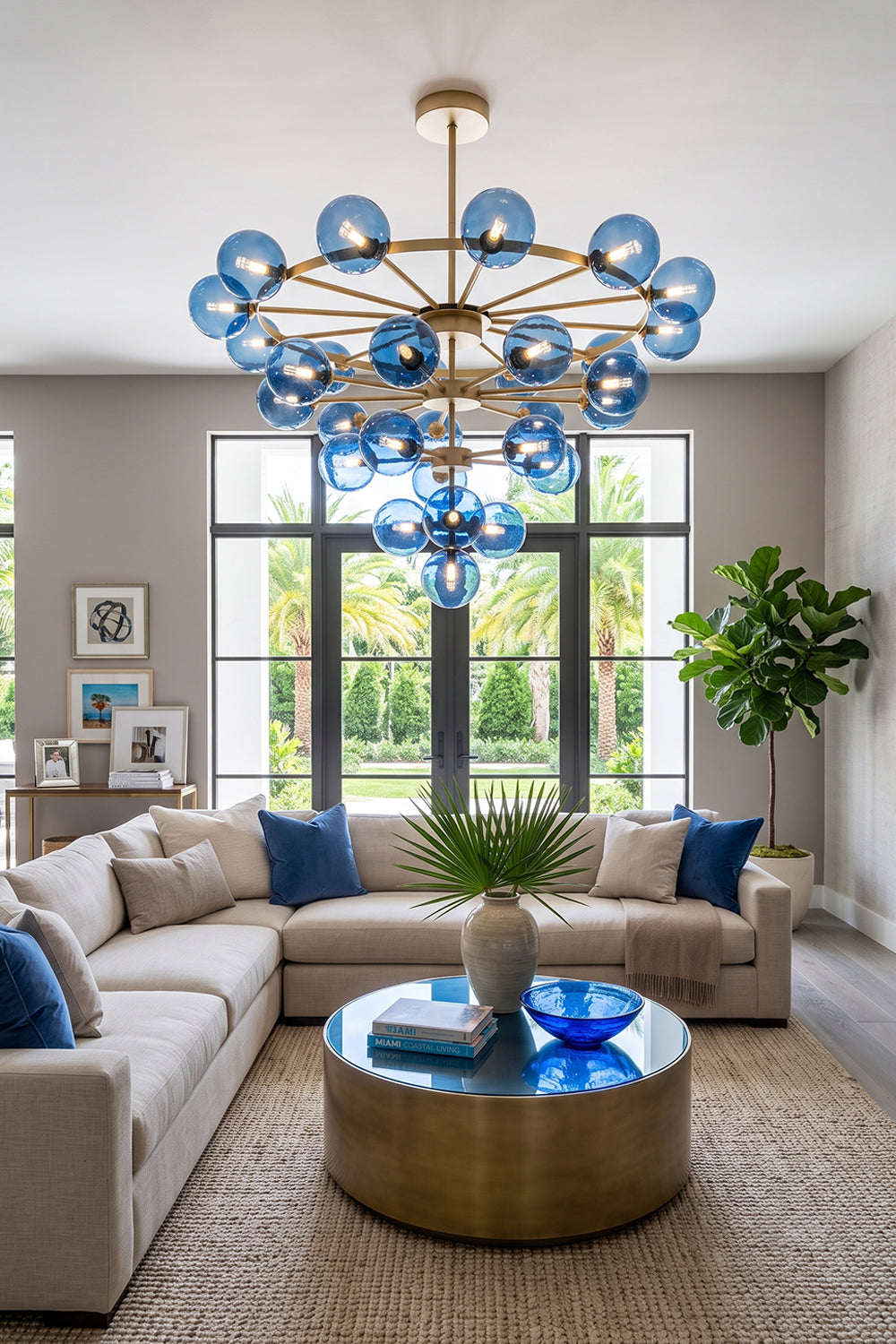 Blue Glass Bubble Globe Tiered Chandelier | Blue Glass and Brass Metal | Styled in a luxury living room corner featuring a large sofa and a matching blue glass coffee table | Samu Lamp