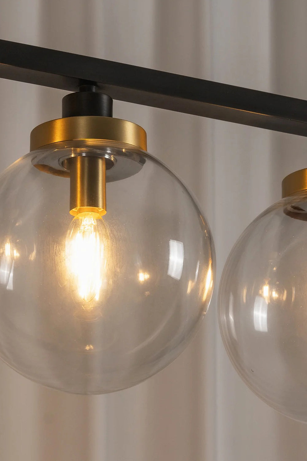 Brooks Linear Glass Globe Chandelier | Glass, Metal | Macro close-up view of a fully illuminated clear glass globe sphere highlighting the warm glowing bulb filament and gold brass cap | Detail shot | Samu Lamp
