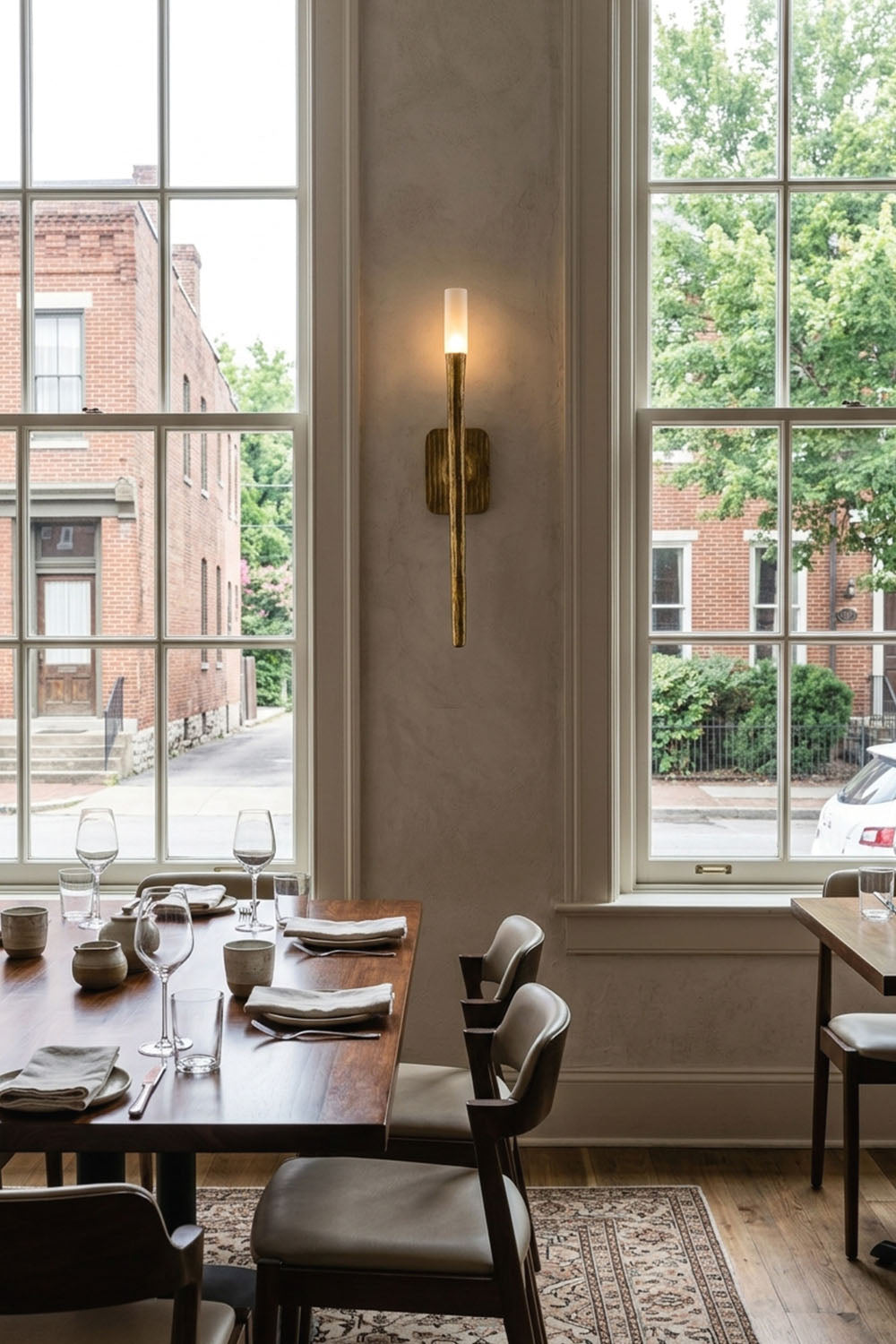 Bryony Torch Alabaster Brass Wall Lamp illuminating a stylish restaurant dining area with large windows.