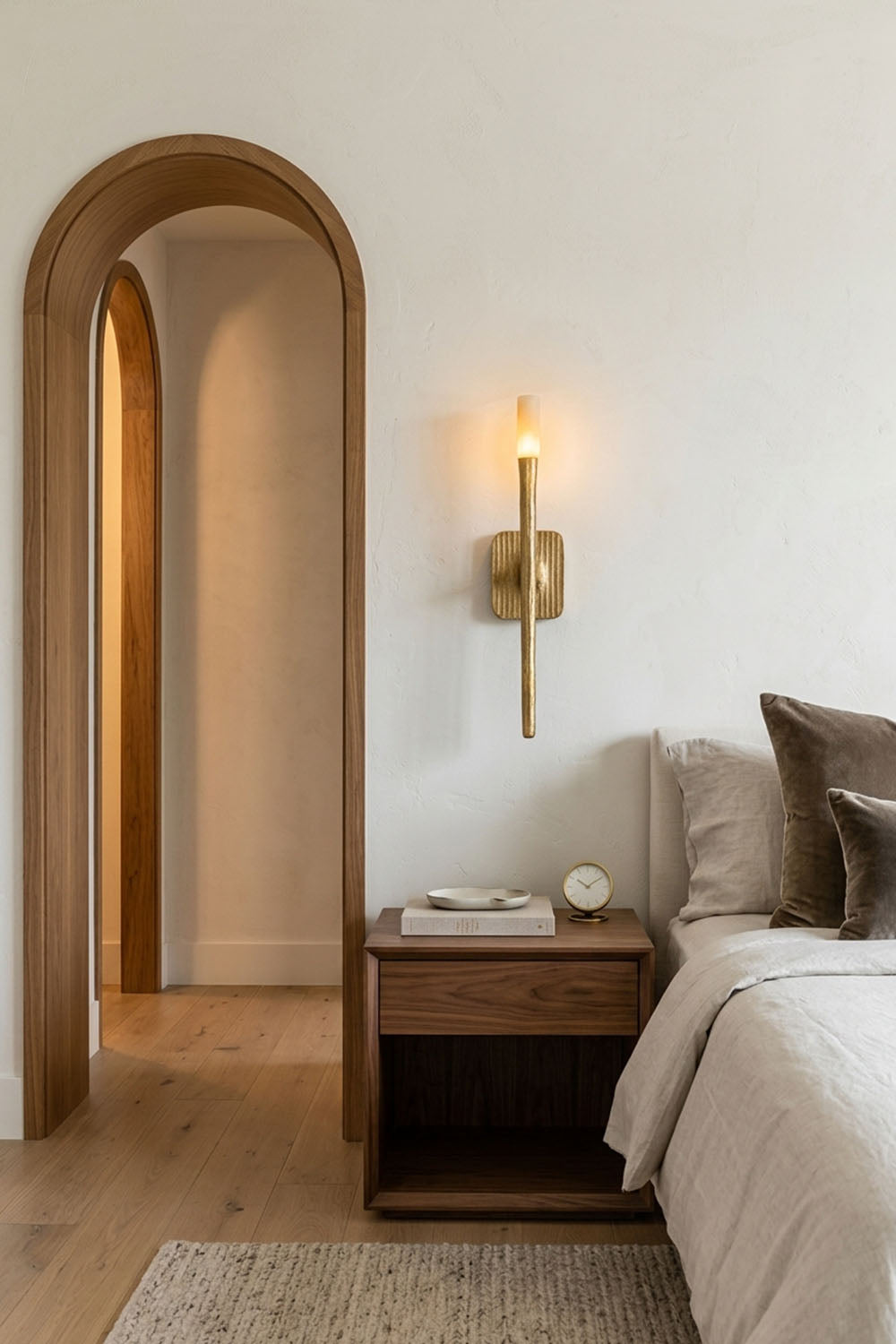 Bryony Torch Alabaster Brass Wall Lamp illuminating a stylish bedroom beside a wooden nightstand.